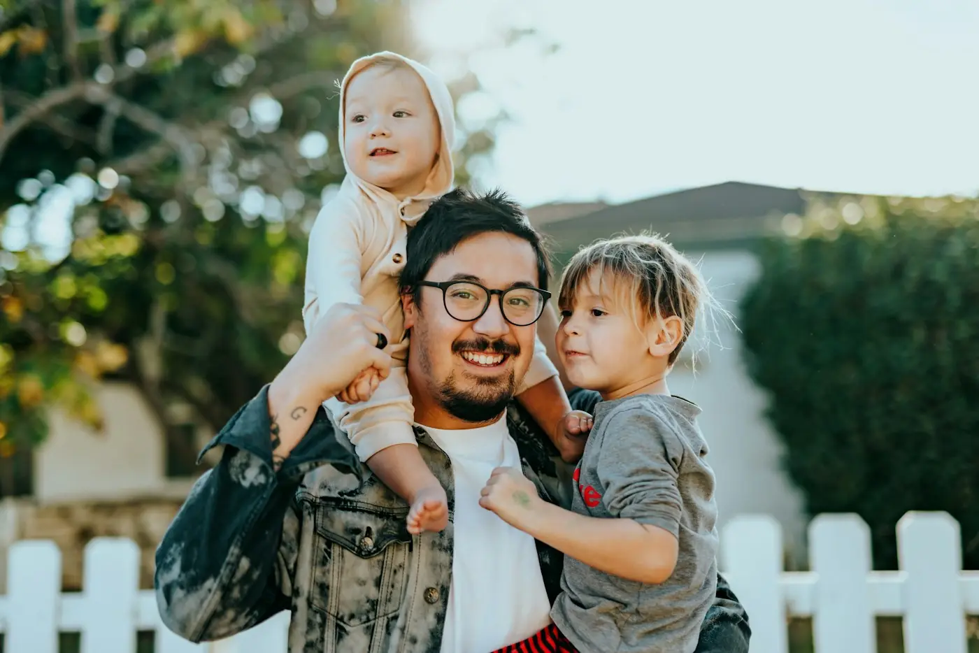 Hombre sonriente carga a dos niños en un jardín familiar